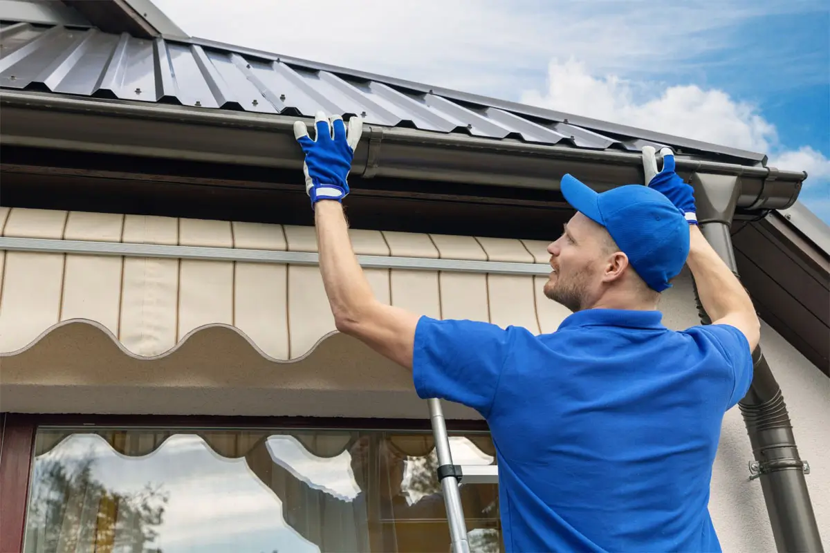 Male worker installing house roof rain gutter system.